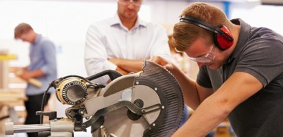 Student And Teacher In Carpentry Class Using Circular Saw