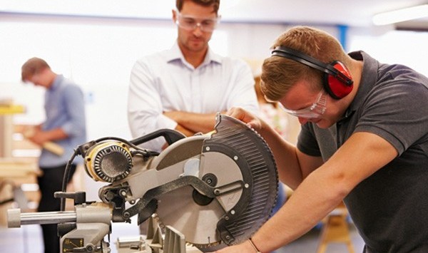 Student And Teacher In Carpentry Class Using Circular Saw